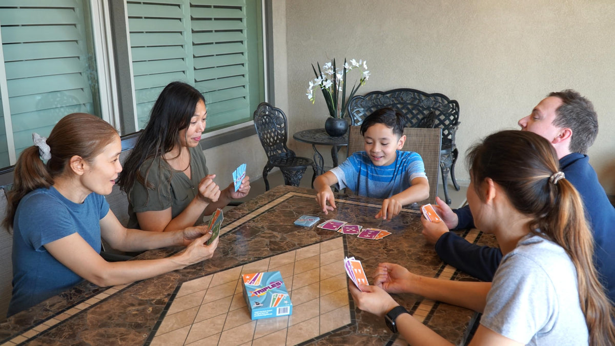 Dad Bomb Games Triples family game night scene with friends.