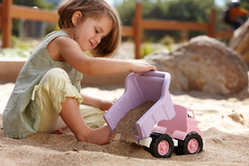 Green Toys pink dump truck outdoors with sand, durable and easy to clean.