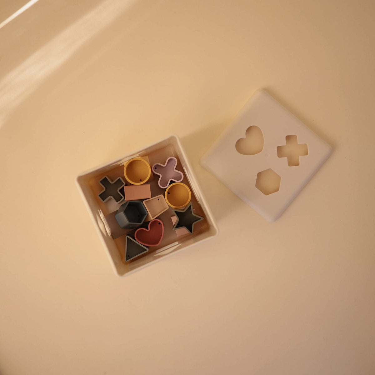 Mushie Shape Sorting Box with 12 shapes supports shape recognition and fine motor practice.