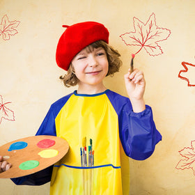 Zkptops child wearing art smock while painting at table.